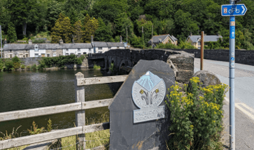 The border of Snowdonia is marked with a decorative stone beside the Dyfi Bridge outside Machynlleth. A fingerpost points out the National Cycle Route 8.